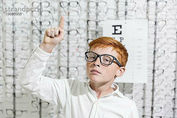 Junge mit Brille zeigt nach oben Richtung stehen gegen Brillen Display Hintergrund