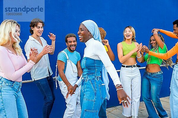 Muslimische junge Frau tanzt in einem Tanzkampf mit Freunden vor einer blauen Wand als Hintergrund