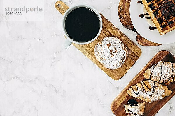 Erhöhte Ansicht Kaffeetasse gebackene Brötchen Croissant Waffeln Holztablett gegen Marmor strukturierten Hintergrund