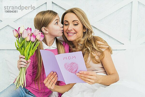 Tochter küsst Mutter mit Grußkarte