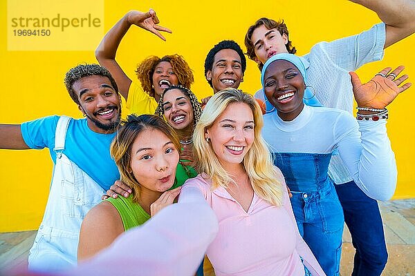 Blonde Frau macht ein Selfie mit multiethnischen Freunden vor einem gelben Hintergrund