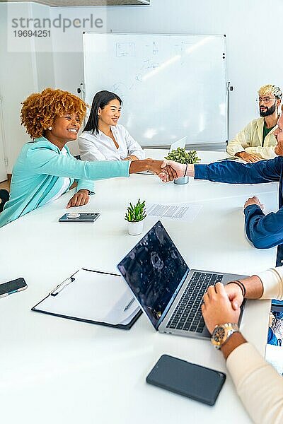Vertikales Foto von multiethnischen Menschen  die sich bei einem Treffen in einem Coworking Center die Hand geben