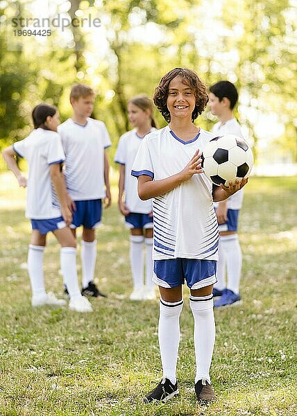 Kleiner Junge hält Fußball außerhalb anderer Kinder