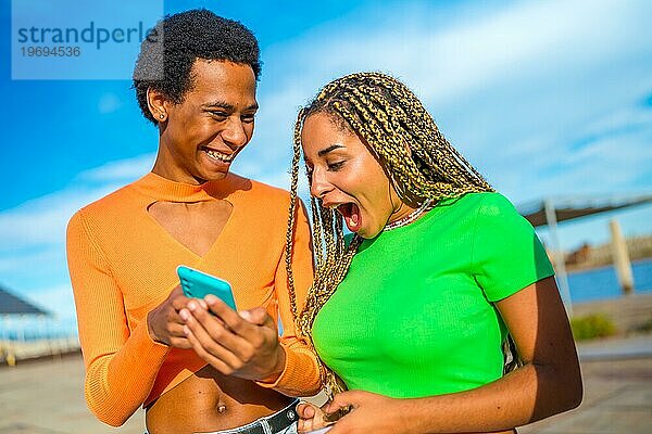 Transgender Person und Afro Frau teilen sich ein Mobiltelefon und lachen im Freien