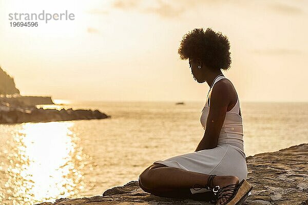 Ruhige Szene einer Afro Frau mit Blick auf das Meer bei Sonnenuntergang