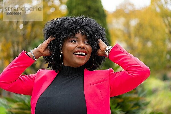Stilvolle afroamerikanische Geschäftsfrau posiert fröhlich im Freien in einem Stadtpark
