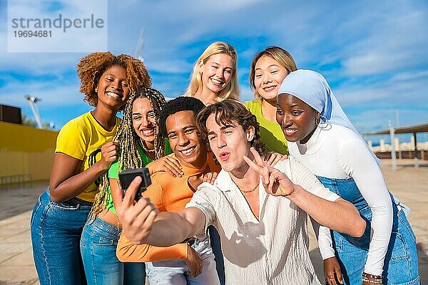 Multiethnische und geschlechtsspezifische Freunde gestikulieren erfolgreich  während sie ein Selfie machen
