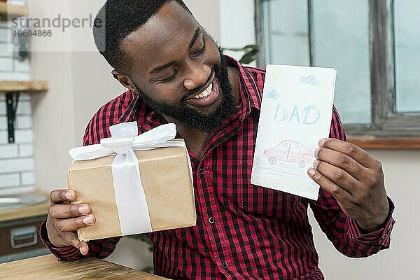 Glücklicher schwarzer Mann hält Grußkarte Geschenk