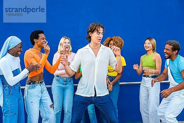 Junger Mann tanzt in einer Tanzschlacht mit Freunden vor einer blauen Wand als Hintergrund