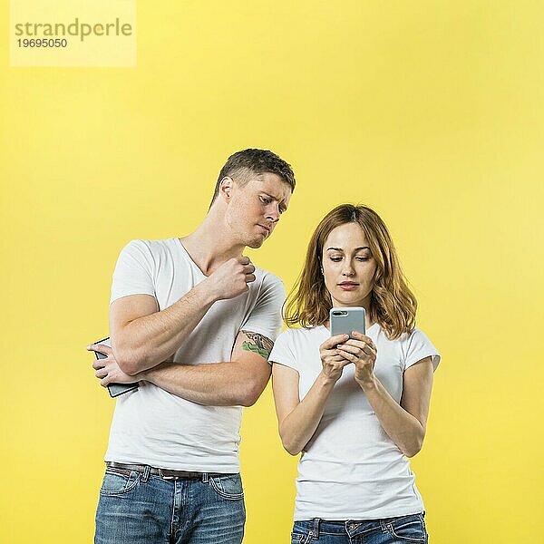 Eifersüchtiger Freund spioniert seine Freundin beobachten ihr Telefon gegen gelben Hintergrund