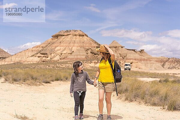 Horizontale Frontalansicht einer Mutter und eines Mädchens  die sich an den Händen halten und in einem trockenen Nationalpark spazieren gehen