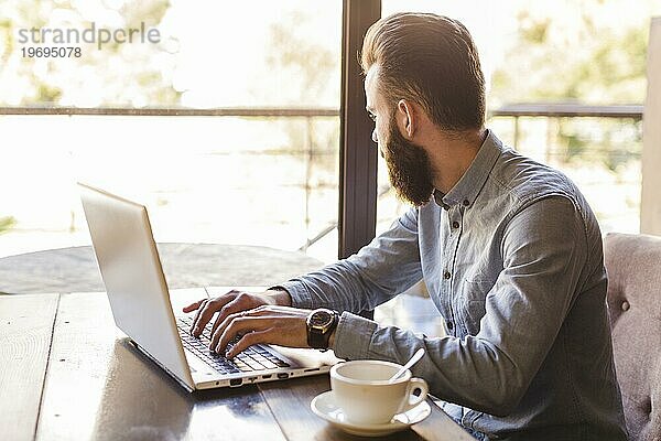 Seitenansicht Mann tippt Laptoptastatur mit Tasse Kaffee Schreibtisch