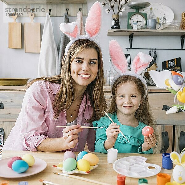 Glückliches Mädchen mit Mutter malt Eier Ostern