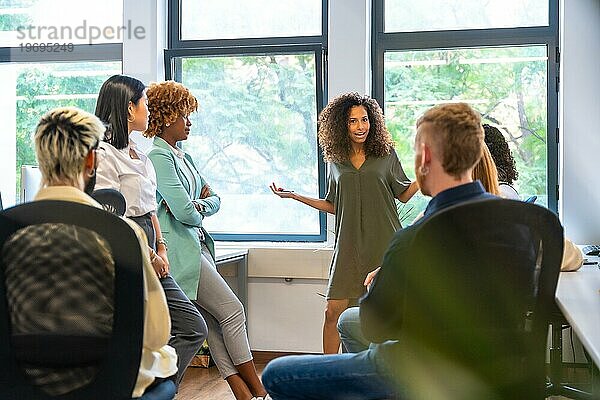Frau leitet ein Treffen mit multiethnischen jungen Menschen in einem Coworking Center