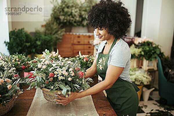 Glückliche afrikanische Frau arrangiert Korb Blumen Schreibtisch