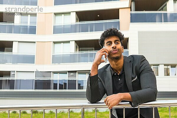 Foto mit niedrigem Blickwinkel und Kopierbereich eines selbstbewussten jungen Unternehmers im Gespräch mit dem Handy im Freien