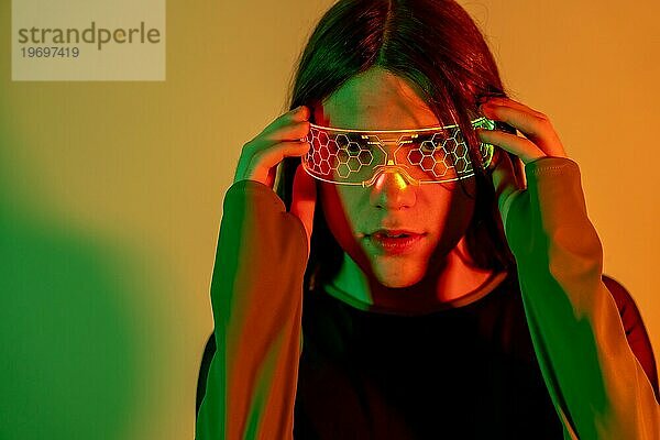 Futuristisches Studioporträt mit Neonlicht einer Transgender Person  die in die Kamera schaut  während sie eine Augmented Reality Brille benutzt