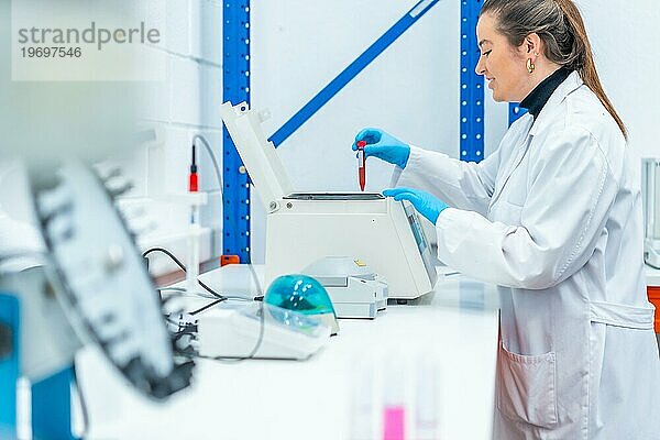 Seitenansicht eines lächelnden Wissenschaftlers  der eine Blutprobe in eine Zentrifuge in einem Forschungslabor einlegt
