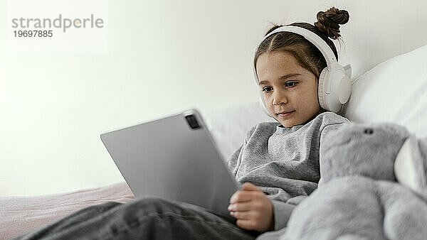 Kleines Mädchen im Bett mit Kopfhörern und Tablette 2