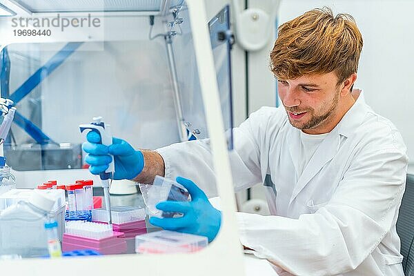 Seitenansicht eines jungen und fröhlichen Wissenschaftlers  der medizinische Proben in eine Mikroplatte im Labor pipettiert