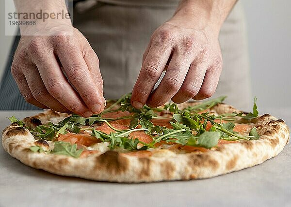 Vorderansicht Mann legt Rucola gebackenen Pizzateig mit geräucherten Lachsscheiben
