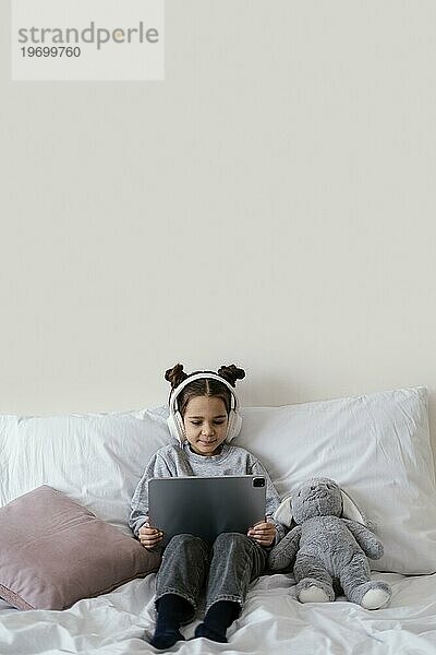 Kleines Mädchen Bett mit Kopfhörern mit Tablet 3