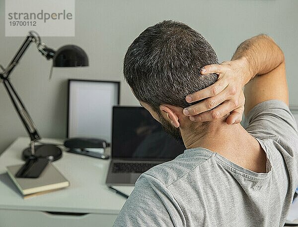 Rückenansicht eines Mannes  der sich bei der Arbeit von zu Hause aus streckt