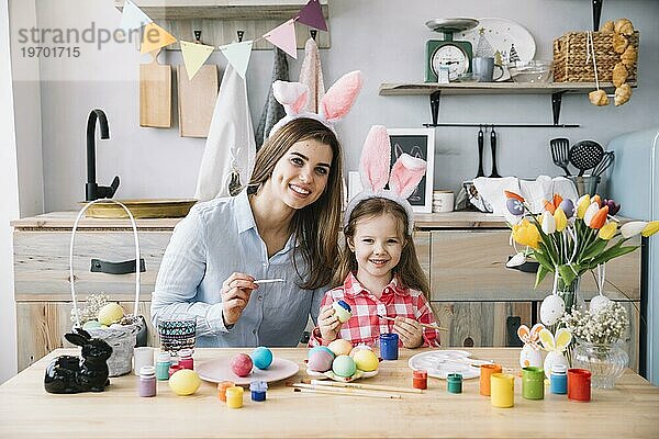 Nettes kleines Mädchen Hasenohren malen Eier Ostern mit Mutter