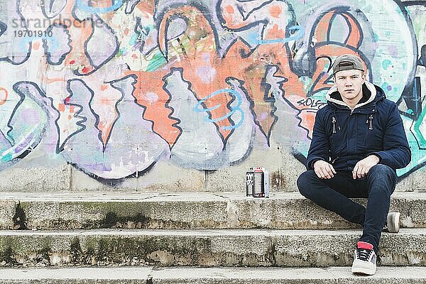 Mann sitzt vor Graffitiwand
