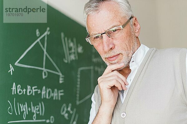 Älterer Professor in der Nähe von Kreidetafel Klassenzimmer stehen