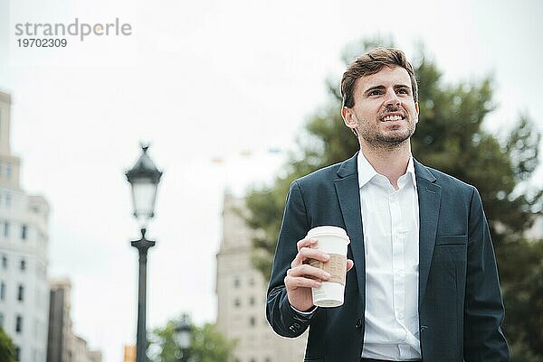 Porträt lächelnder junger Geschäftsmann  der eine Tasse Kaffee zum Mitnehmen in der Hand hält