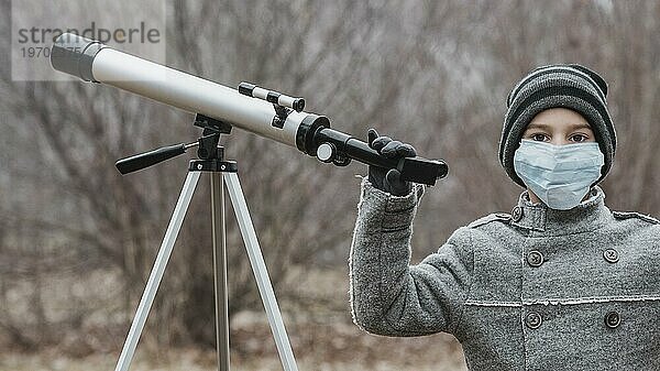 Kleiner Junge mit medizinischer Maske und Teleskop