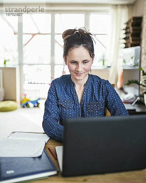 Lächelnde Frau  die zu Hause am Laptop arbeitet