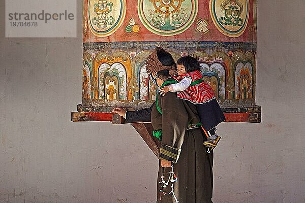 Eine tibetische Frau mit Kind dreht eine der riesigen Gebetsmühlen an der Sengze Gyanak Manimauer entlang der Sichuan Tibet Straße zwischen Yushu und Xiewu  Provinz Qinghai  China  Asien