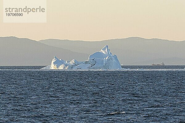 Ein Eisberg schwimmt in der aufgehenden Morgensonne vor der Silhouette der Berge der grönländischen Küste. Diskobucht  Grönland  Dänemark  Nordamerika