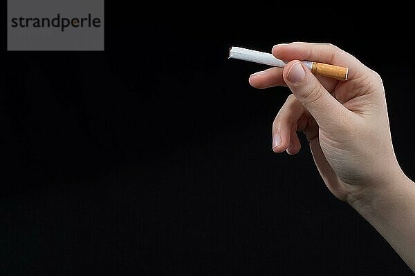 Hand hält eine Zigarette auf schwarzem Hintergrund