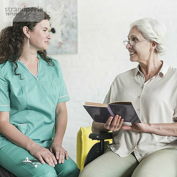 Attraktive Krankenschwester suchen ältere Frau Patientin sitzt Rollstuhl mit Buch