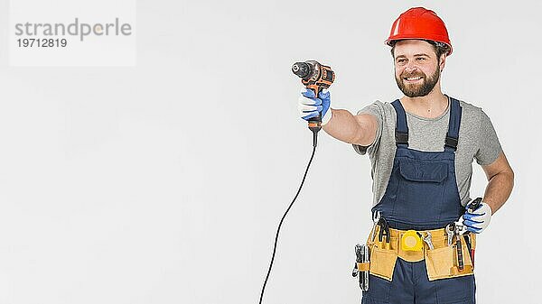 Glücklicher Mechaniker im Overall mit Bohrer in der Hand