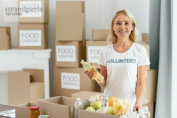 Lächelnde freiwillige Helferin bei der Vorbereitung einer Kiste mit Lebensmittelspenden