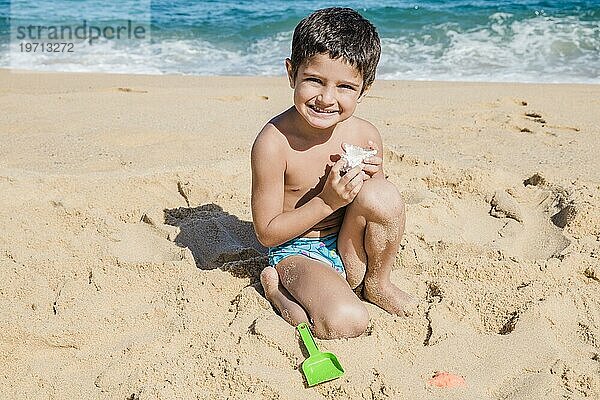 Junge spielt mit Muschel Strand