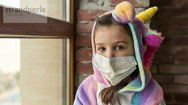 Kleines Mädchen im Dinosaurieranzug mit Gesichtsmaske während der Quarantäne zu Hause