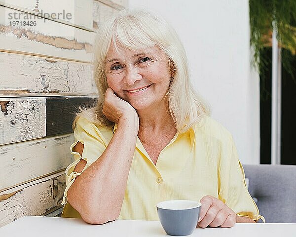 Ältere Frau sitzt in der Küche mit Tasse und lächelt