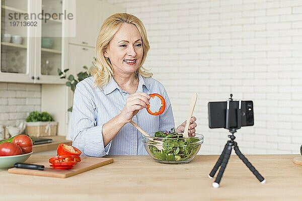 Ältere Frau macht Videoanruf Handy zeigt Paprikascheibe bei der Vorbereitung Salat