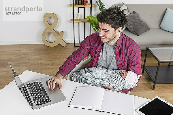 Glücklicher Vater mit Baby am Laptopschreibtisch
