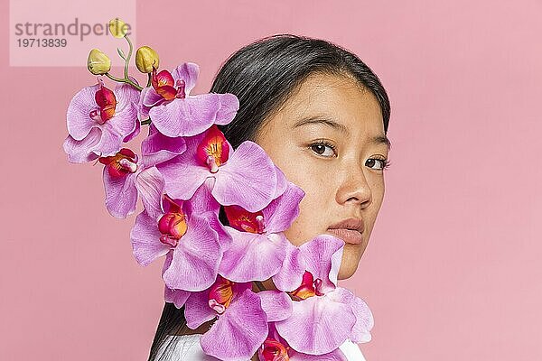 Frau bedeckt ihr Gesicht mit einer Orchidee und schaut in die Kamera