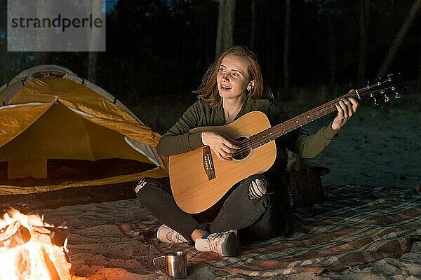 Glückliches Mädchen spielt Gitarre am Lagerfeuer