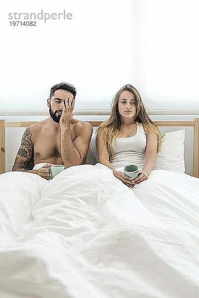 Junges Paar mit Tasse Kaffee im Bett sitzend