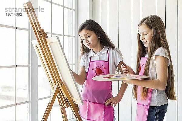 Close up zwei Mädchen stehen in der Nähe von Fenster Malerei Staffelei mit Farbe Pinsel