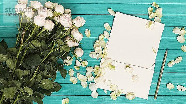 Erhöhte Ansicht weißen Rosen Bleistift leeres Papier Blütenblätter gegen grüne Holztisch