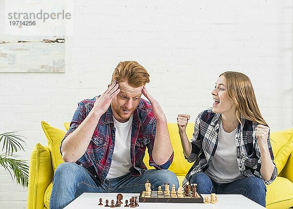 Aufgeregte junge Frau sitzt mit ihrem Freund und jubelt  nachdem sie eine Schachpartie gewonnen hat